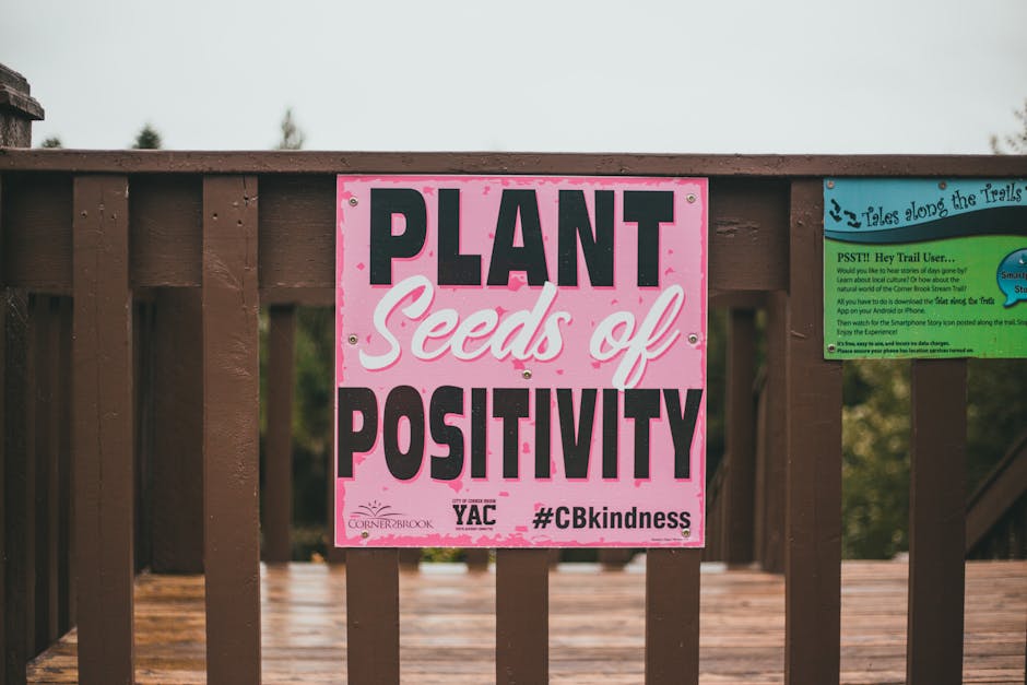 Home Colorful sign promoting kindness and positivity on a wooden railing outdoors.